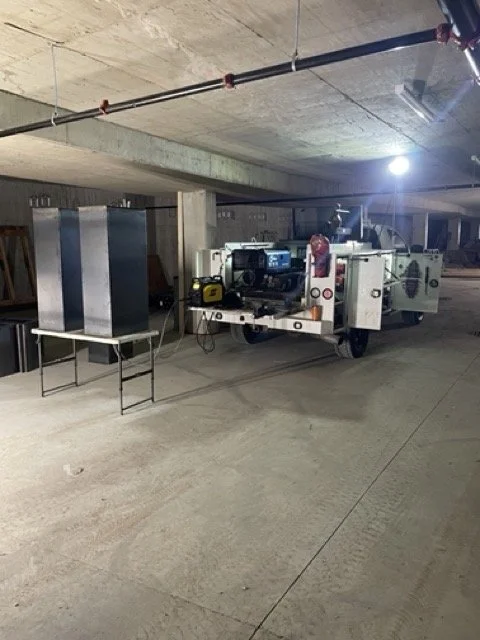 Industrial machinery and equipment in an underground parking garage or basement, with some tools and a worktable nearby.