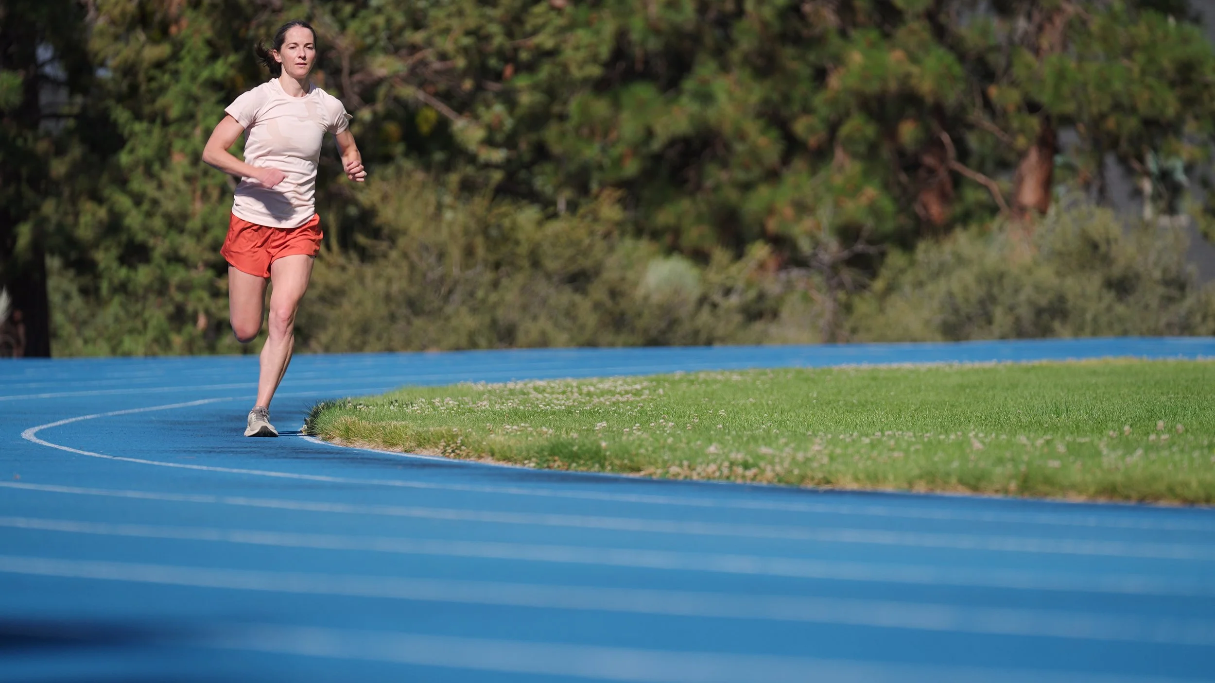 A woman running on a blue outdoor track with grass and trees in the background.