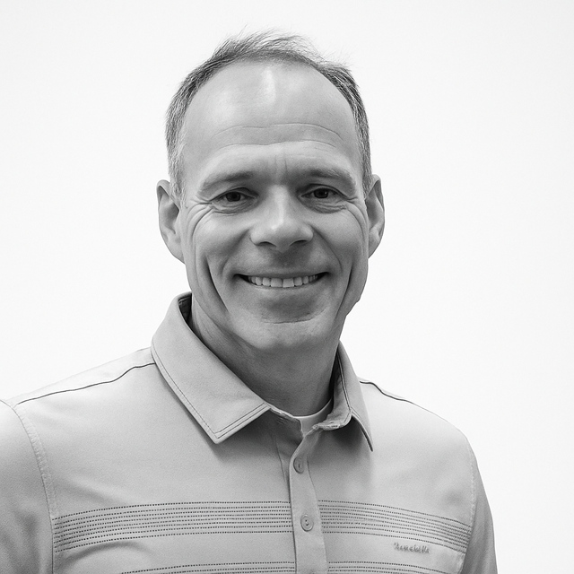 Black and white photo of a smiling man with short hair, wearing a collared shirt against a plain background.