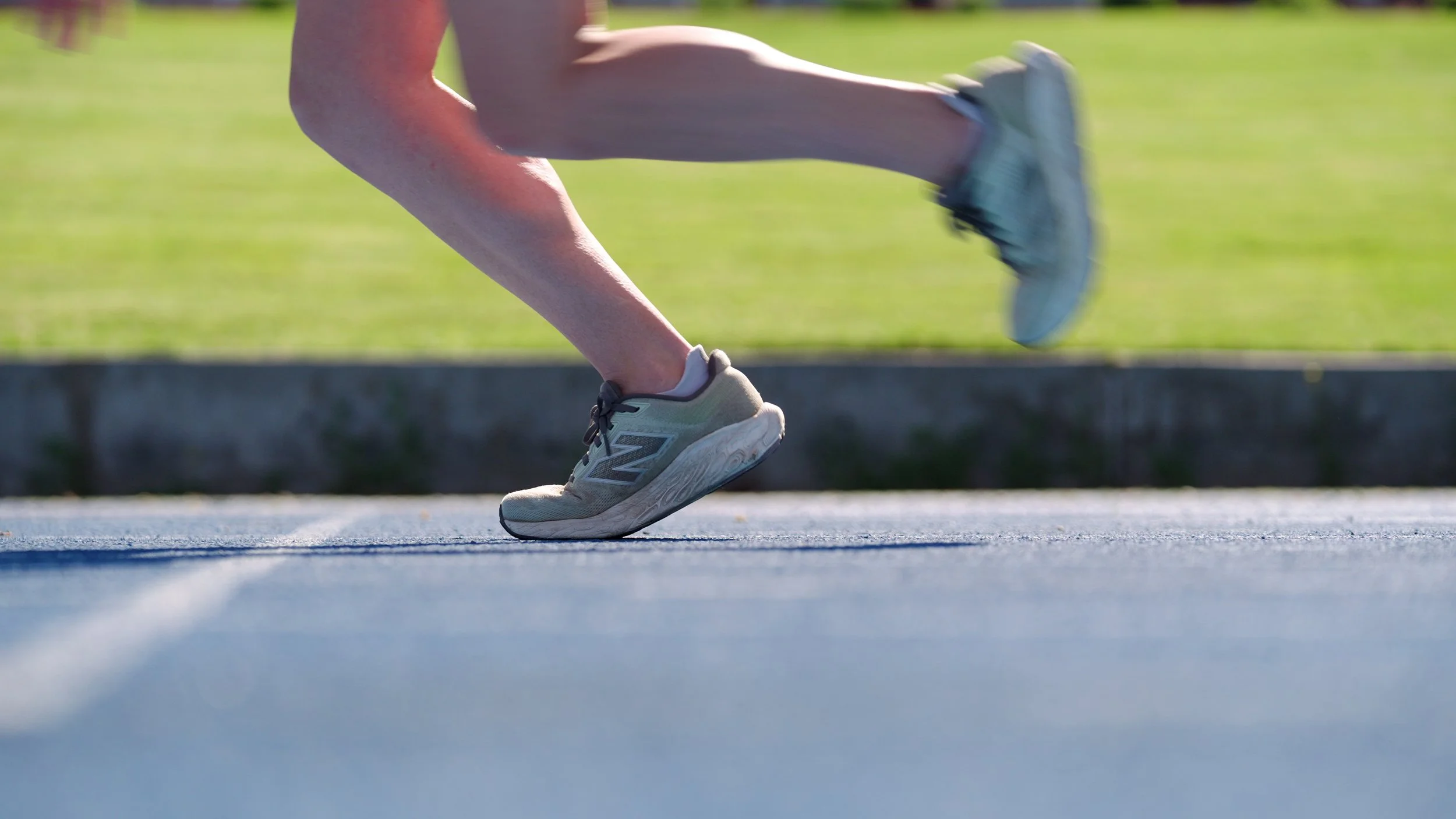 Close-up of a person running on a track, focusing on the legs and shoes, with a grassy field in the background.