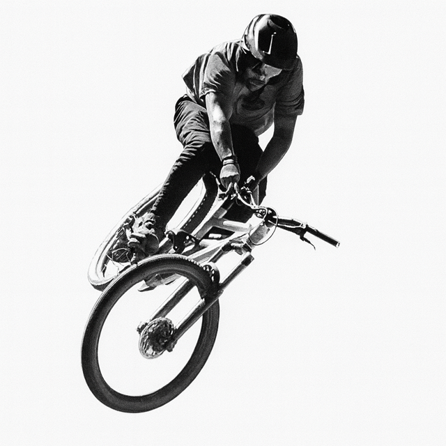A person wearing a helmet riding a mountain bike in mid-air against a plain background.