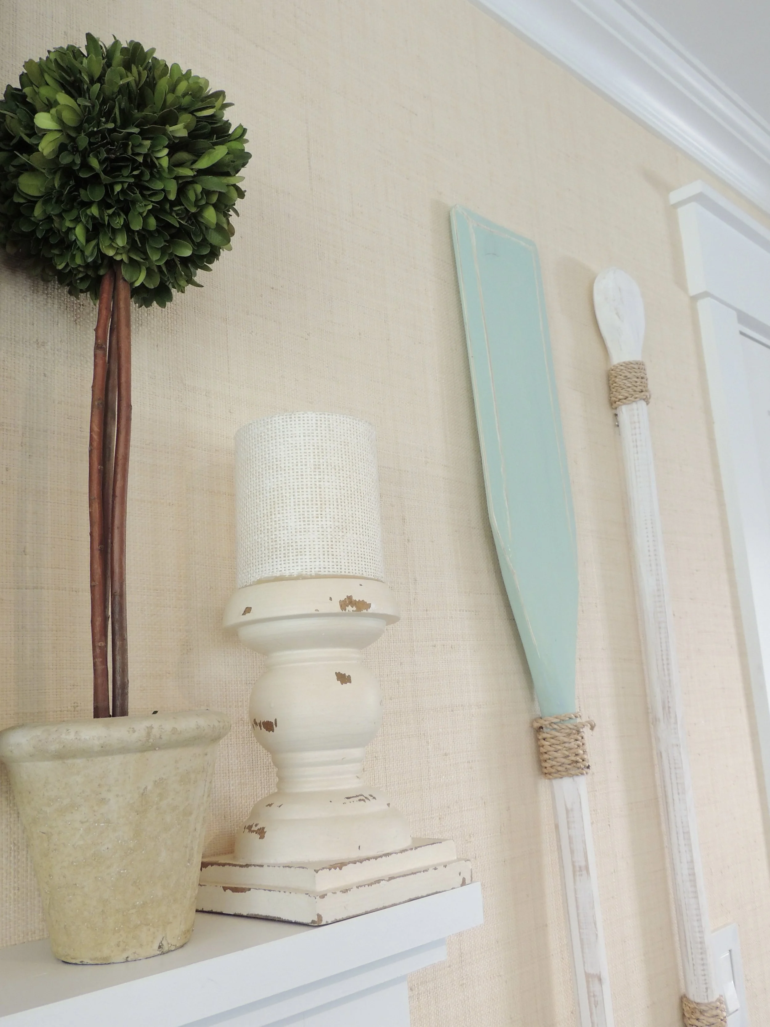 Decorative interior wall with a topiary plant, a distressed white lamp, a painted wooden oar, and a white paddle.