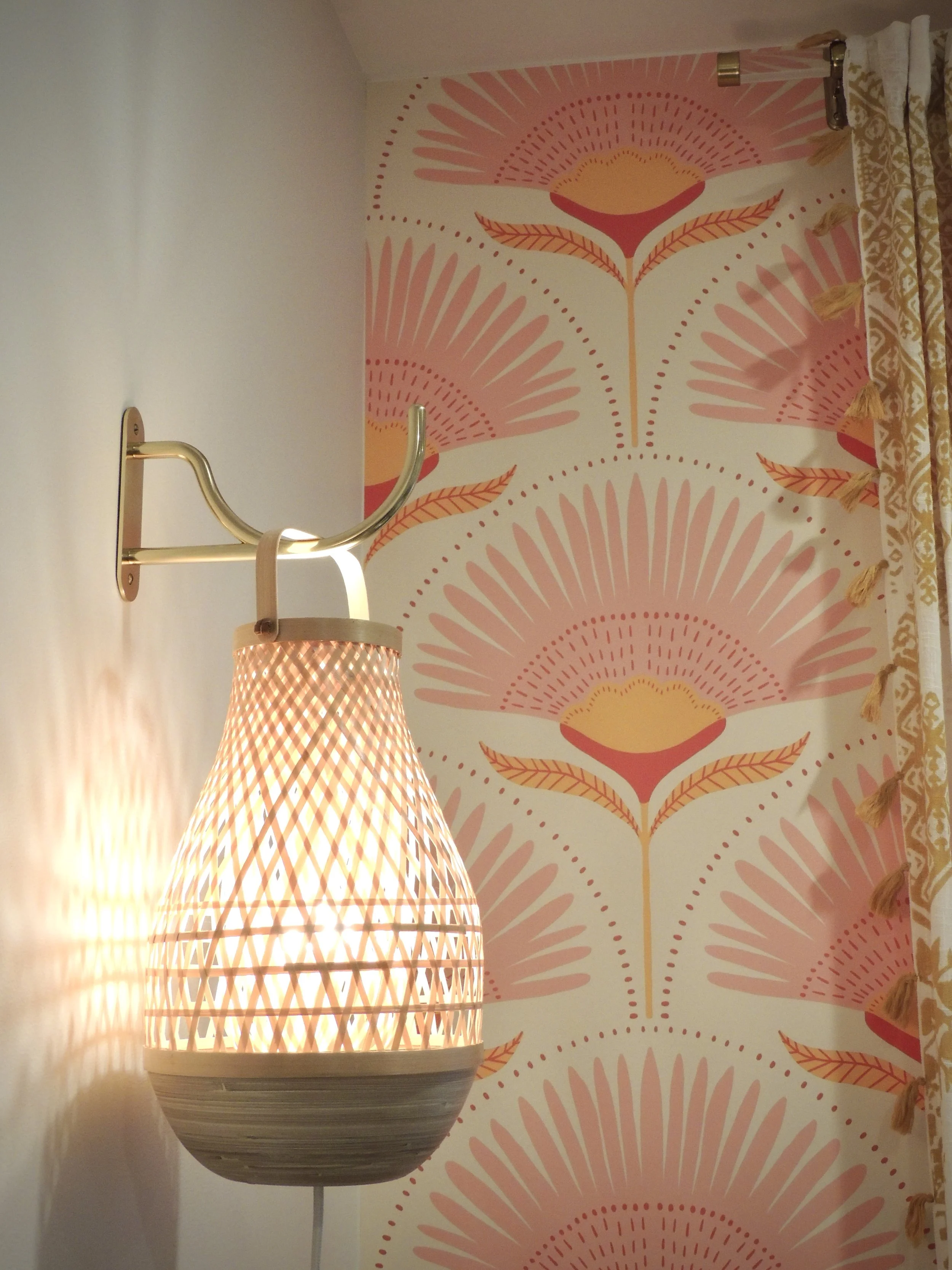 Decorative wall with pink, orange, and yellow floral pattern and a wall-mounted lamp with a woven, lattice-style shade.