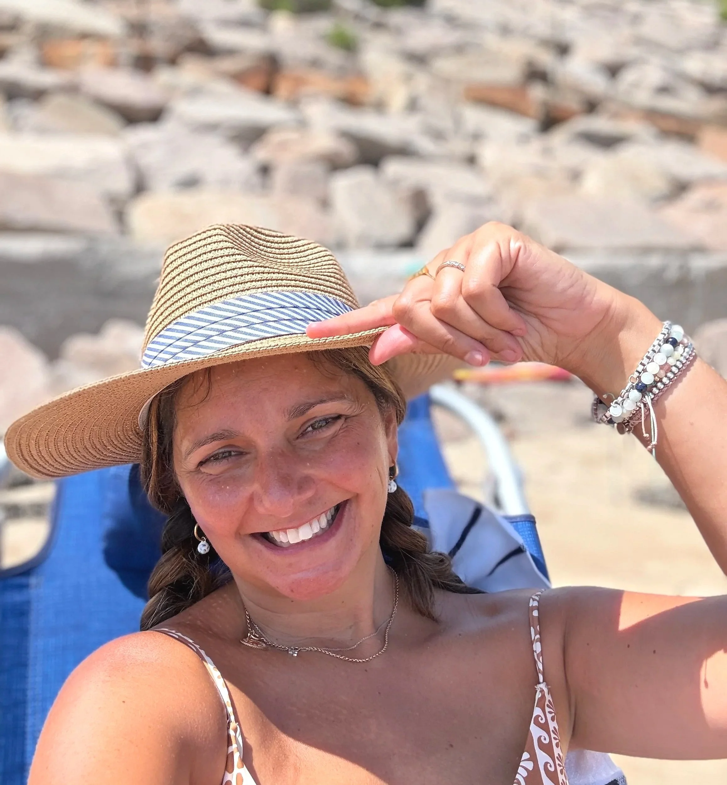 Woman smiling at the beach wearing a sun hat, jewelry, and a summer dress.