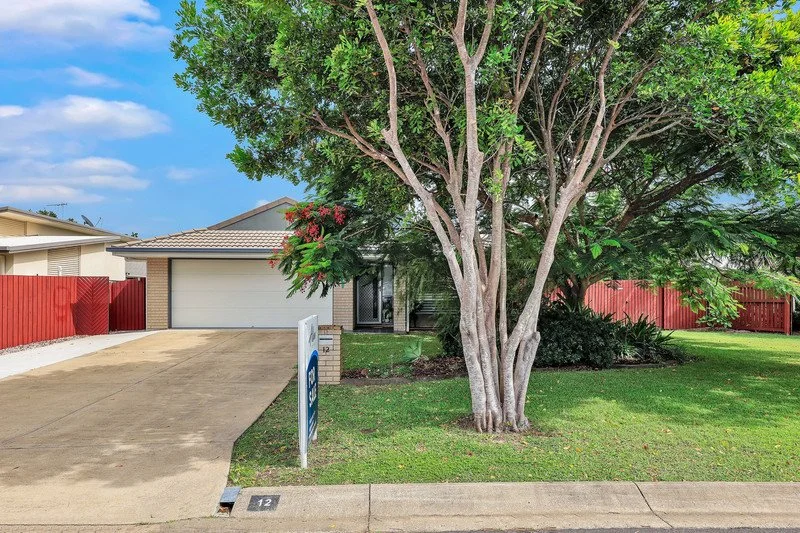 Front yard of a suburban house with a large tree, a driveway, green lawn, and a red fence in the background.