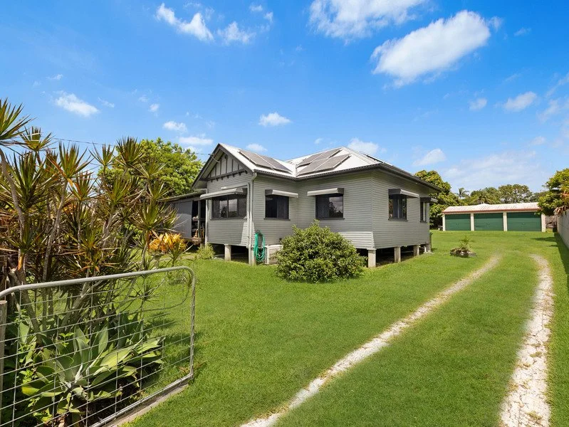 A gray house on a grassy lawn under a bright blue sky with scattered clouds.