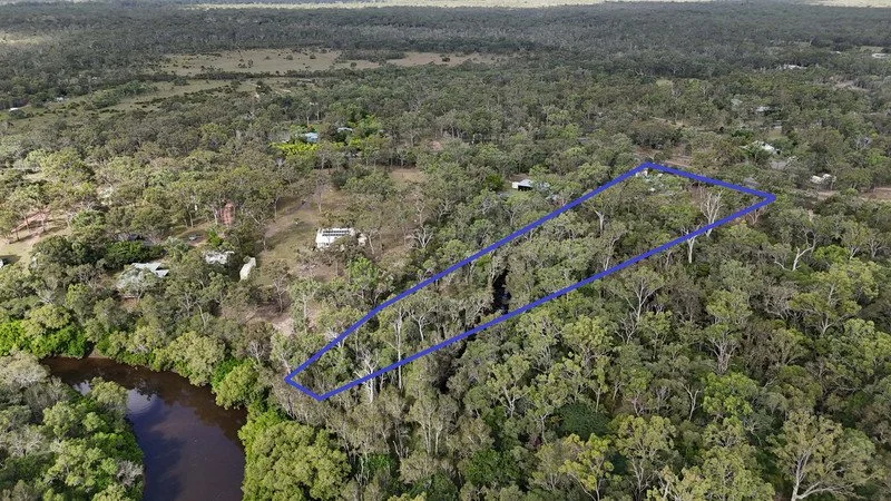 Aerial view of a rectangular plot of land outlined in blue, surrounded by dense forest and a river at the bottom left corner.