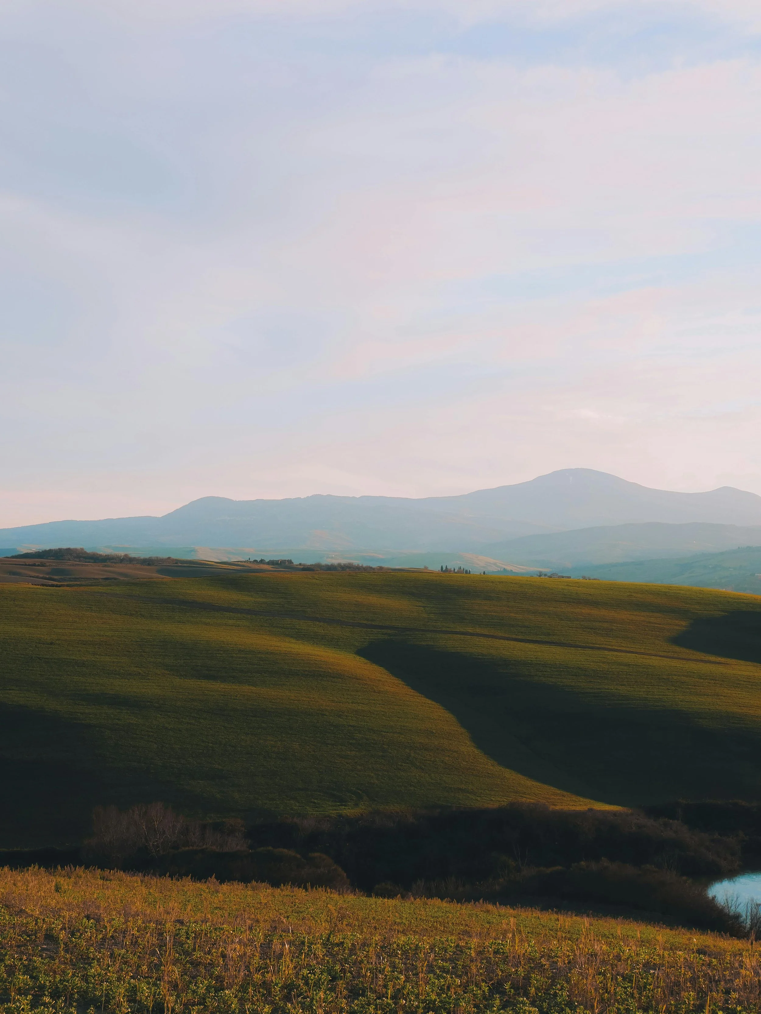 Landscape of rolling green hills with distant mountains under a cloudy sky.