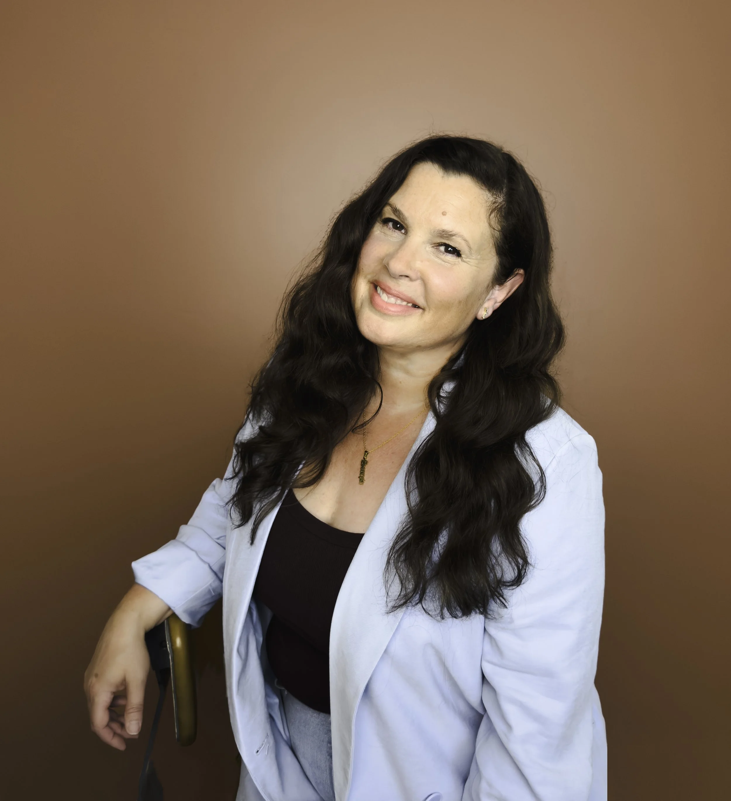Dhana Cartmell Performance Public Speaking coach woman with long dark hair wearing a light blue blazer and a black top smiles against a terracotta background.