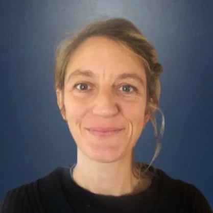 Close-up of a woman with light skin, blonde hair, and blue eyes smiling, against a blue background.