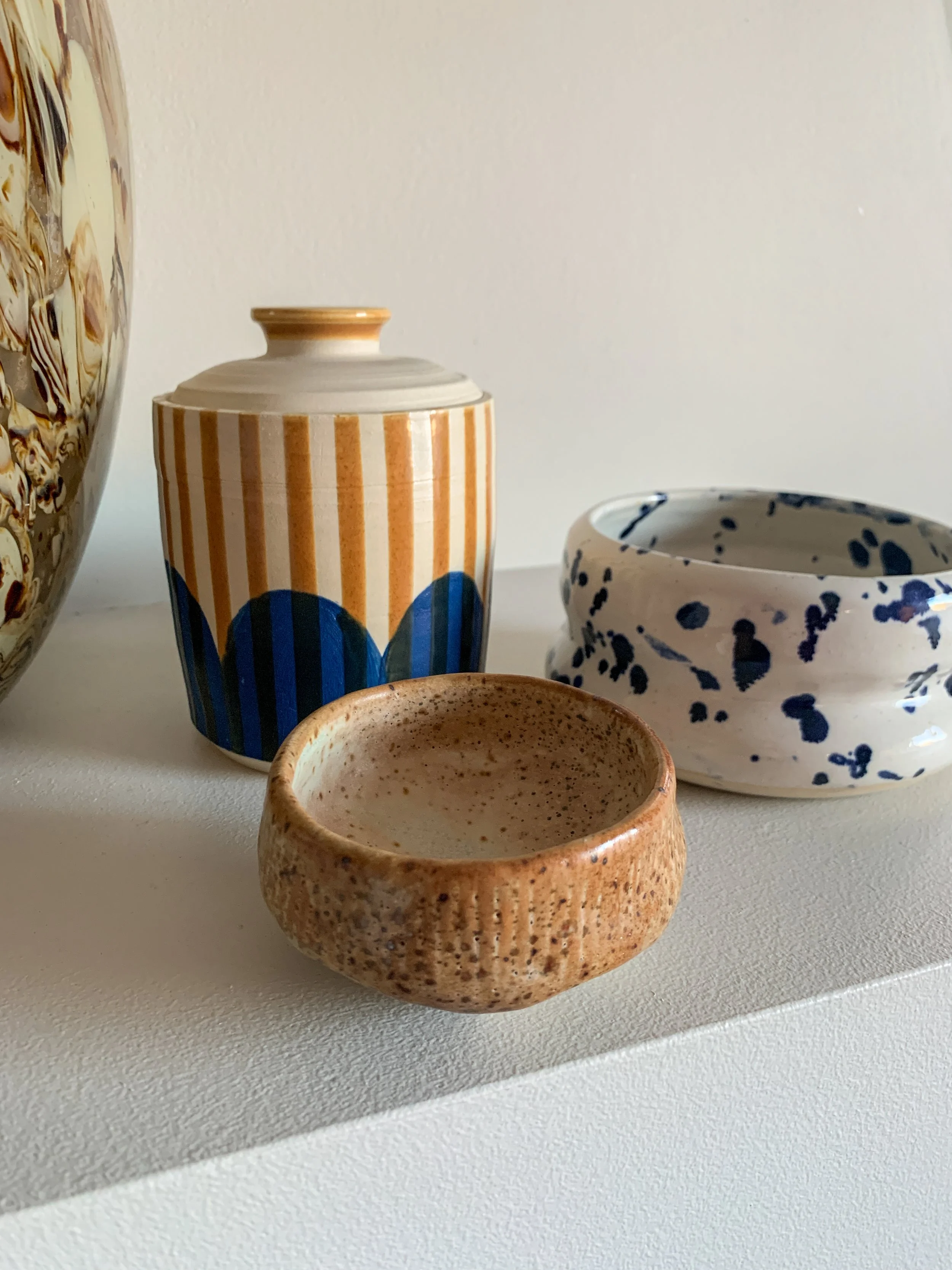 Four ceramic pots of varying shapes and patterns on a white surface. The pots range in color, pattern, and texture, with some featuring stripes, speckles, and splatter designs.
