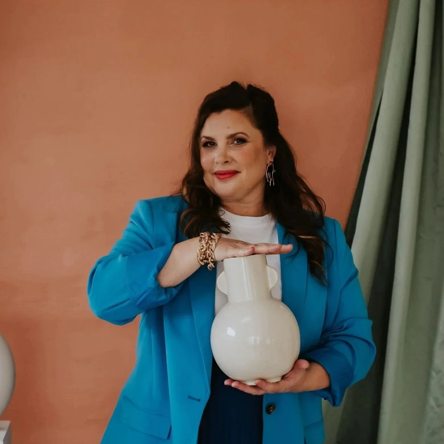 A woman public speaking performance coach in blue blazer with brown hair holds a white vase