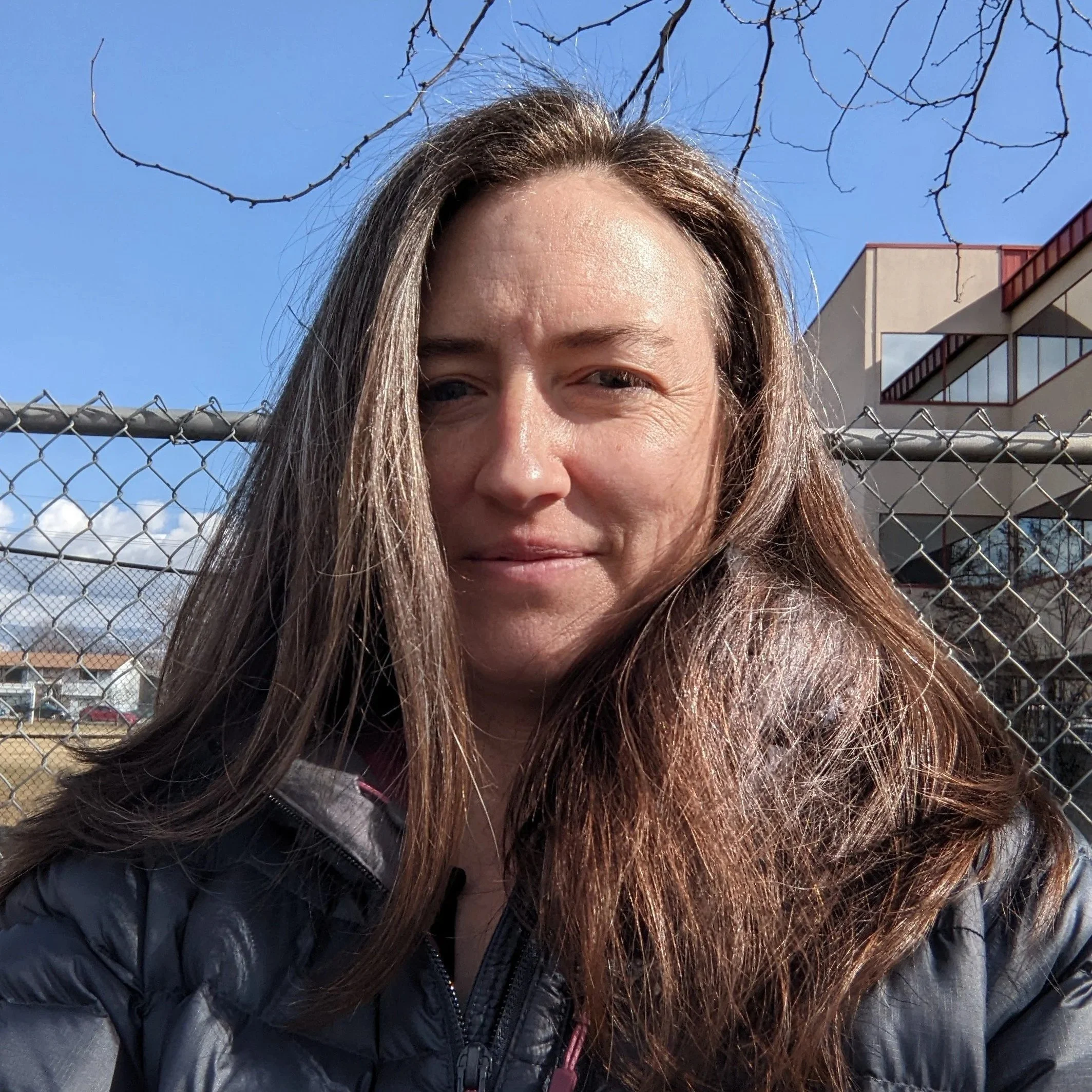 Headshot of a smiling middle-aged woman public speaking coaching and performance client  with brown hair, wearing a coat outdoors with blue sky in the background