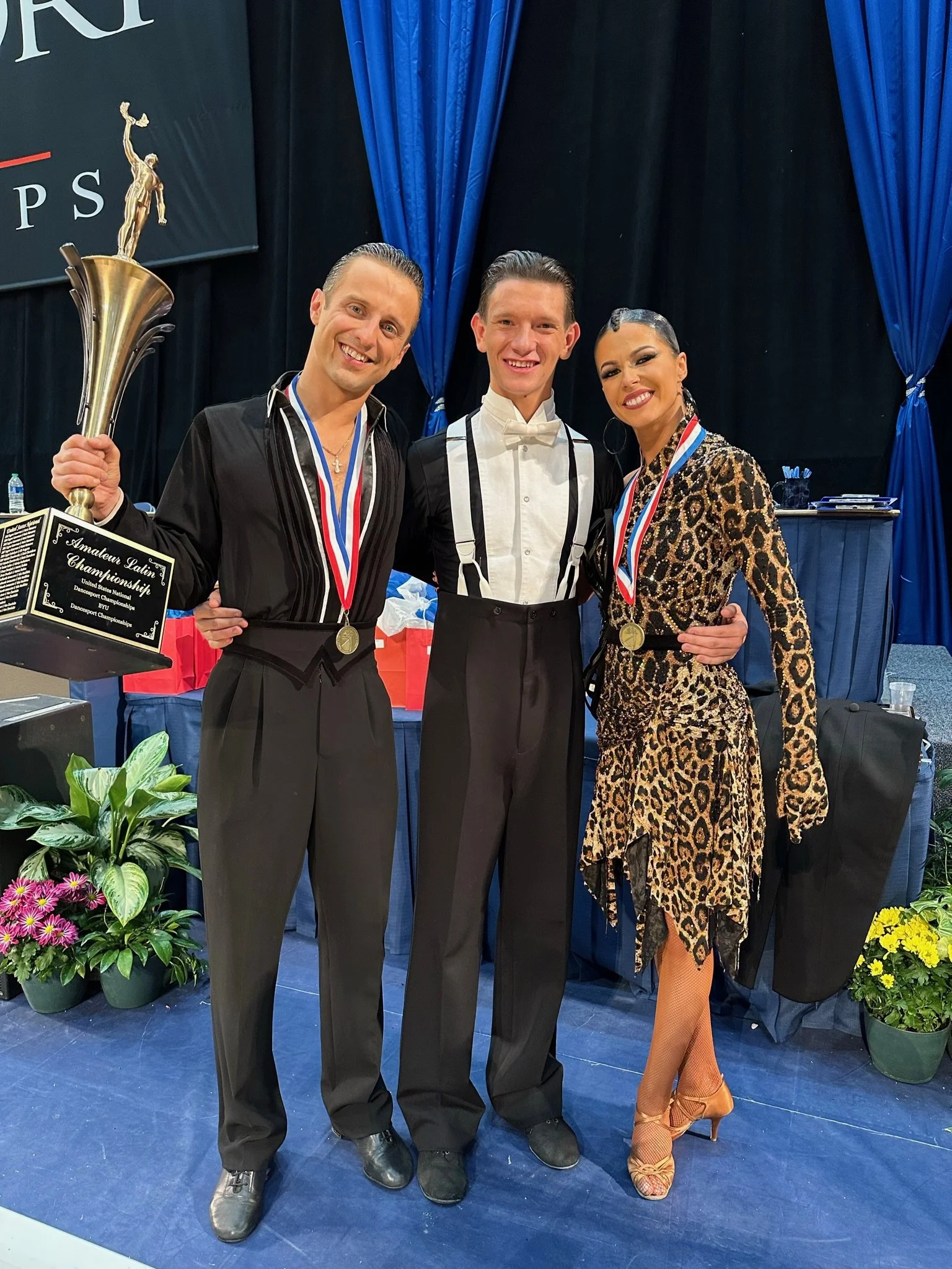 Noah Scribner standing with his World Champion Latin Ballroom coaches after winning an event at the National Amateur DanceSport Championship competition hosted at BYU.