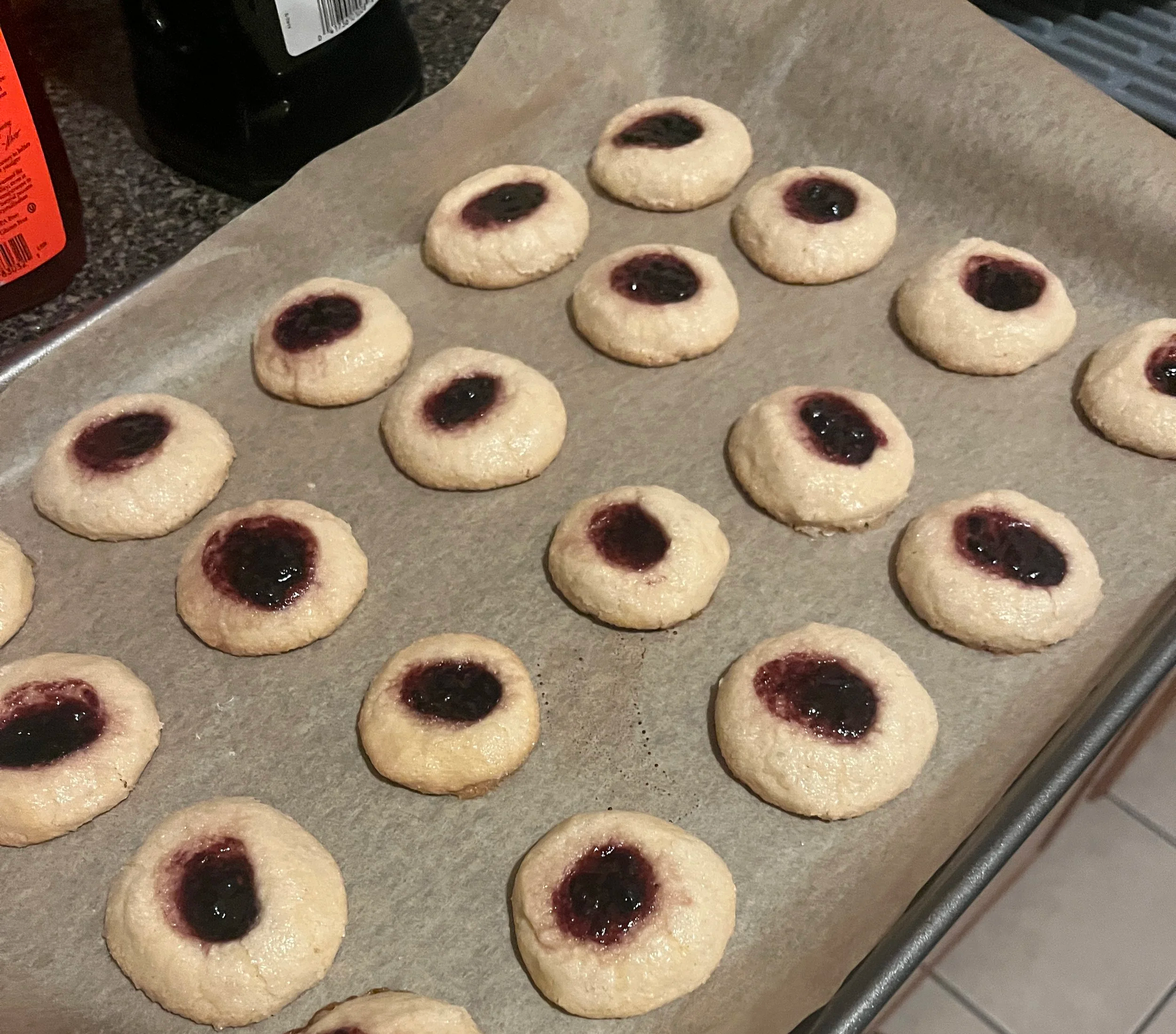 A cookie sheet lined with parchment paper and jam filled thumbprint cookies.