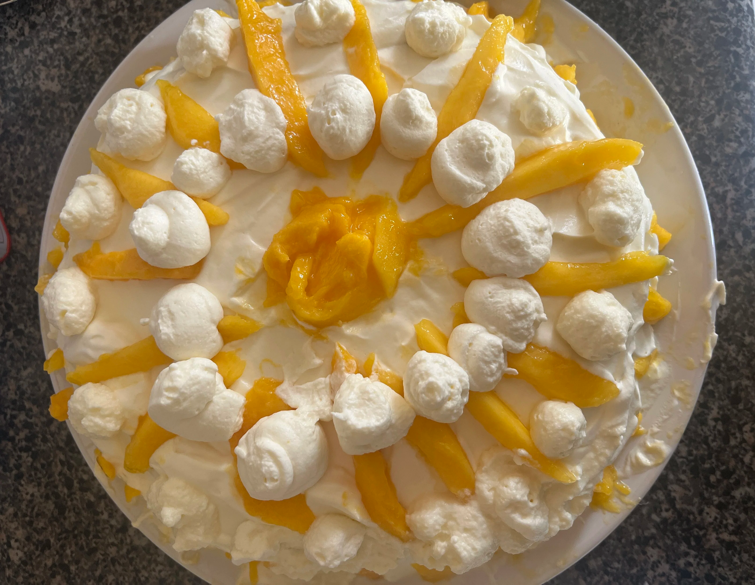 A cake decorated with mango spears and dollops of whipped cream frosting.