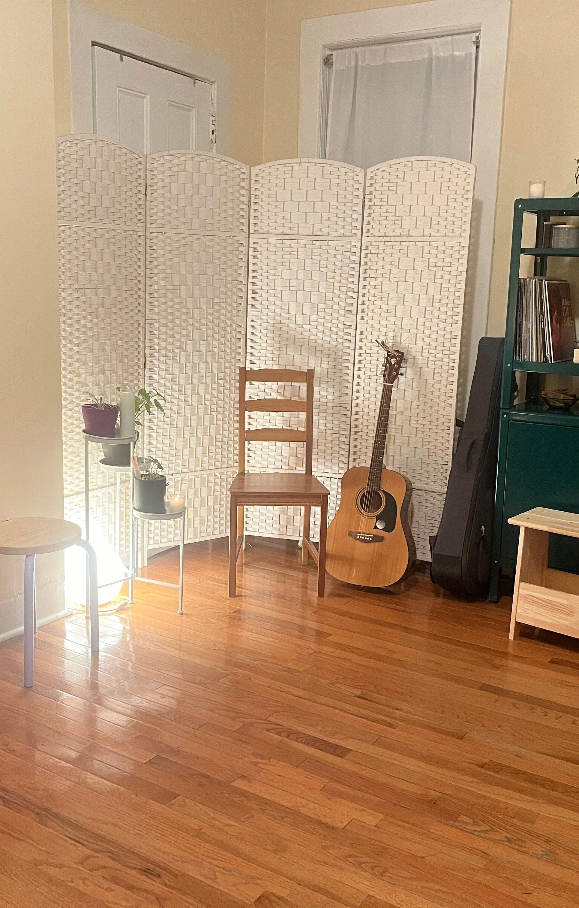 A guitar resting next to a chair and surrounded by plants, and lights.