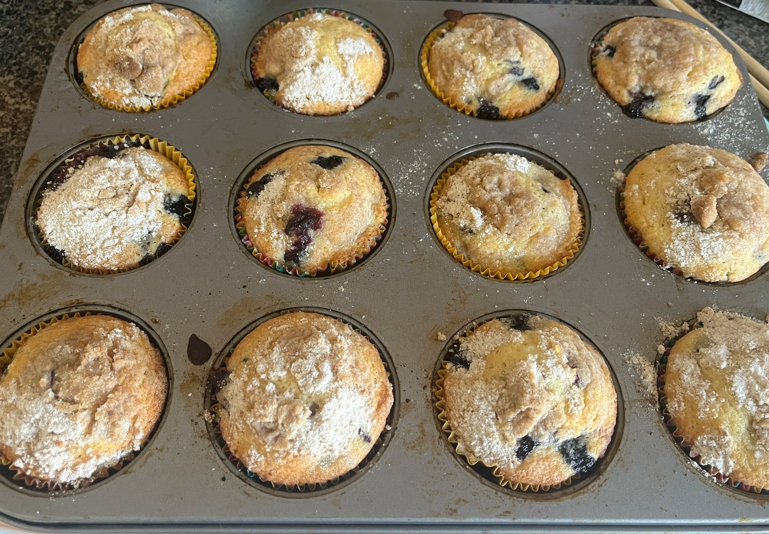 A muffin tin filled with blueberry muffins with crumb topping.