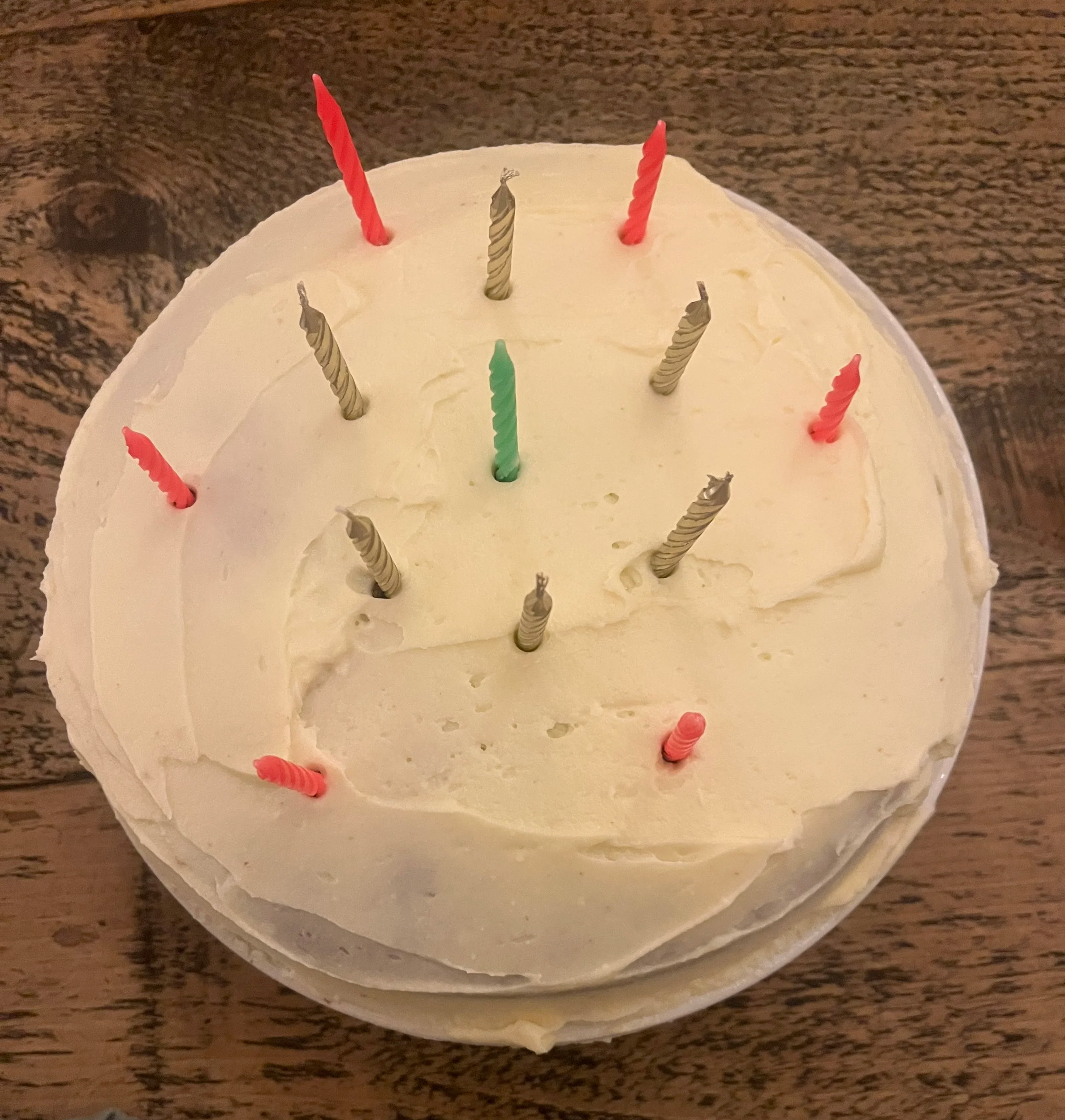 A cake decorated with cream cheese frosting and neon pink, gold, and one neon green candle