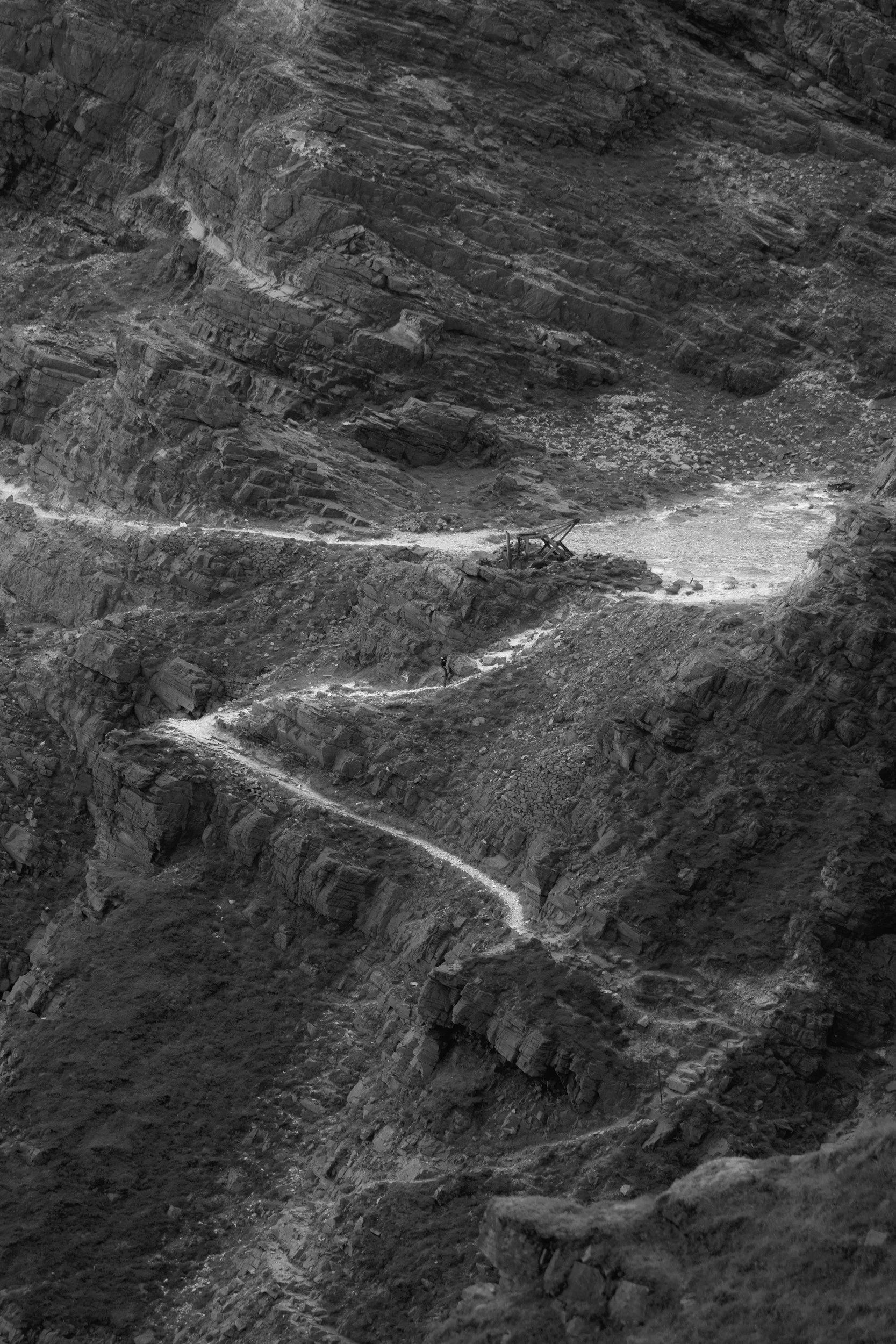 A winding dirt trail carved along a steep mountain ridge with rocky terrain and cliffs on either side.