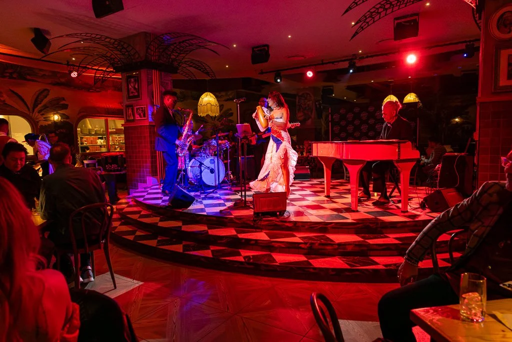 Jazz band performing live on a checkered platform in a dimly lit restaurant with red lighting and an audience seated around