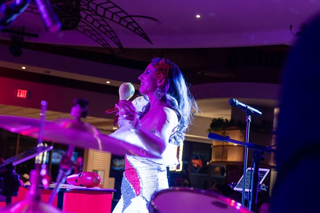 A woman singing and dancing on stage with a tambourine and microphone in a dimly lit venue with purple lighting.
