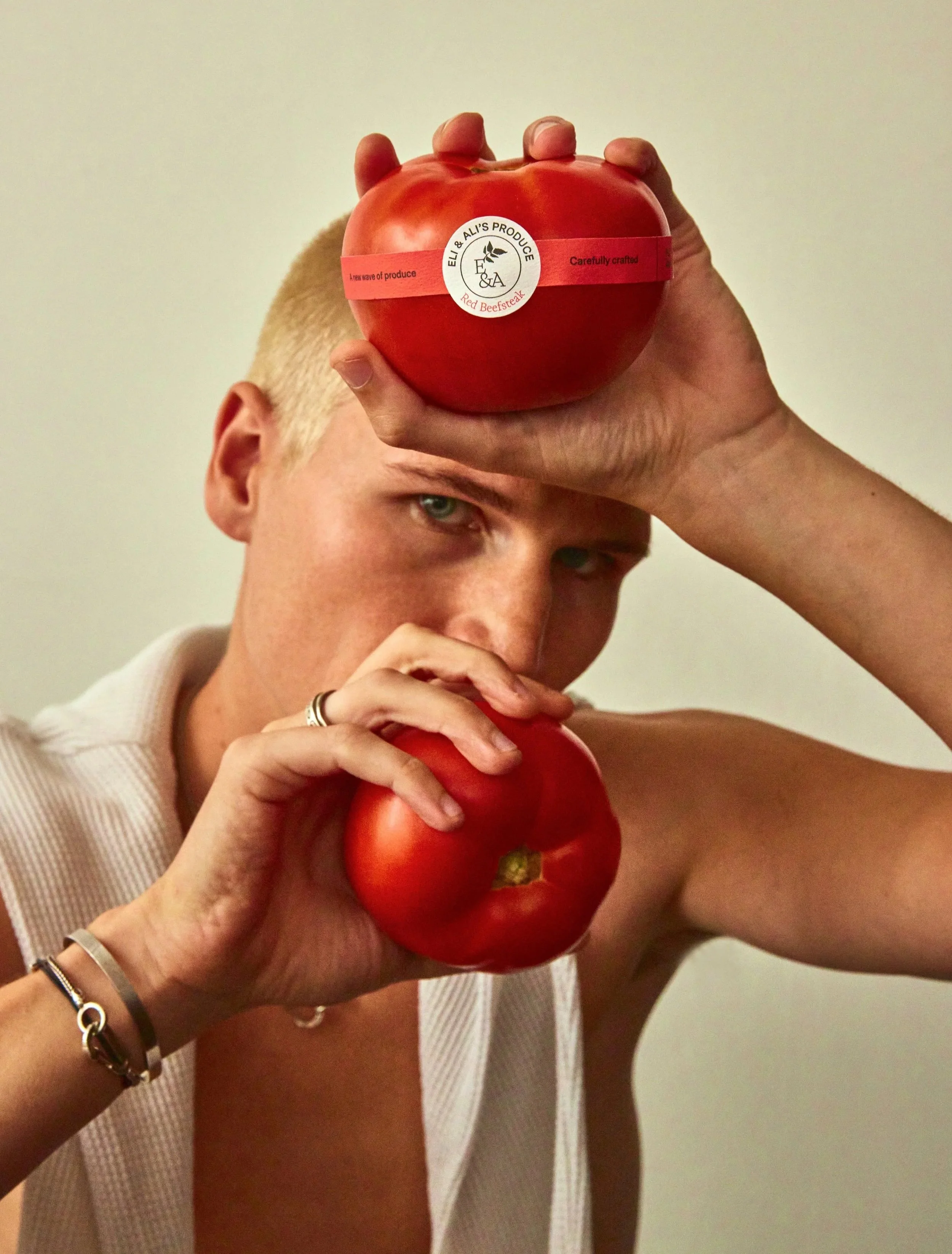 Person holding two large red tomatoes, one on the forehead and one near the face.