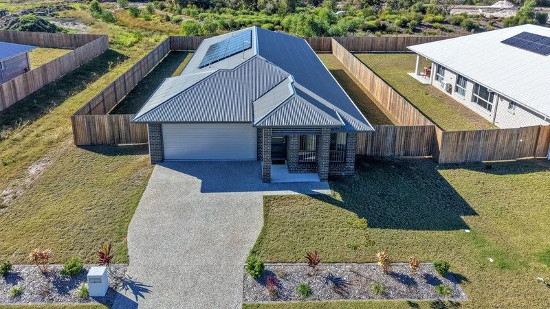A modern house with a gray metal roof and solar panels, fenced backyard, and a concrete driveway, located in a suburban neighborhood.