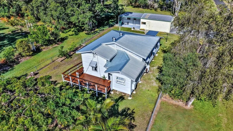 A white house with a metal roof, a wooden deck, and surrounded by green trees and lawn, viewed from above.