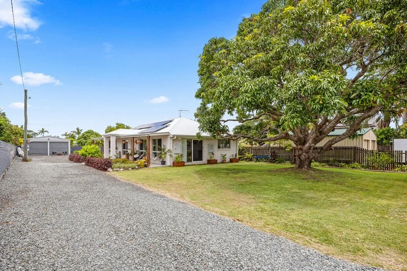 A house with a large front yard, a gravel driveway, and a big tree on the right side.