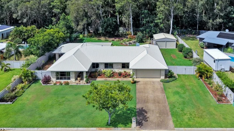 Aerial view of a single-story house with a large front lawn, driveway, white fence, and surrounding trees.