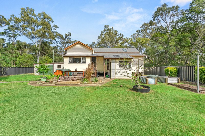 Backyard with a house, green lawn, garden beds, and trees.