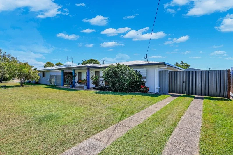 A single-story house with a front lawn, concrete driveway, and a backyard fence under a blue sky with clouds.