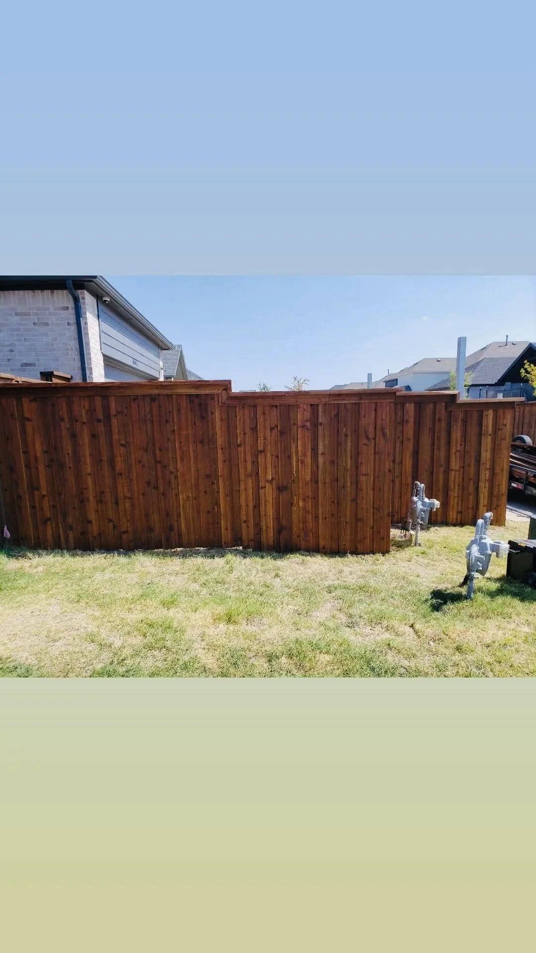 Backyard with a tall wooden fence, green grass, and utility meters.