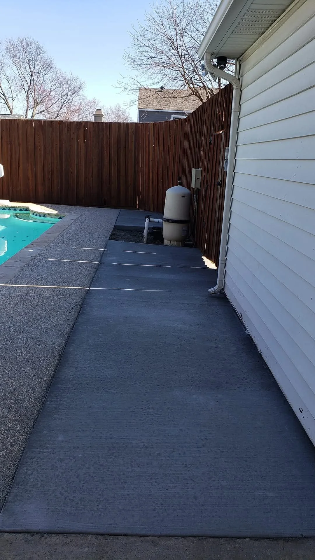 Side yard with a concrete pathway alongside a house, a wooden privacy fence, a pool, and a pool filter.