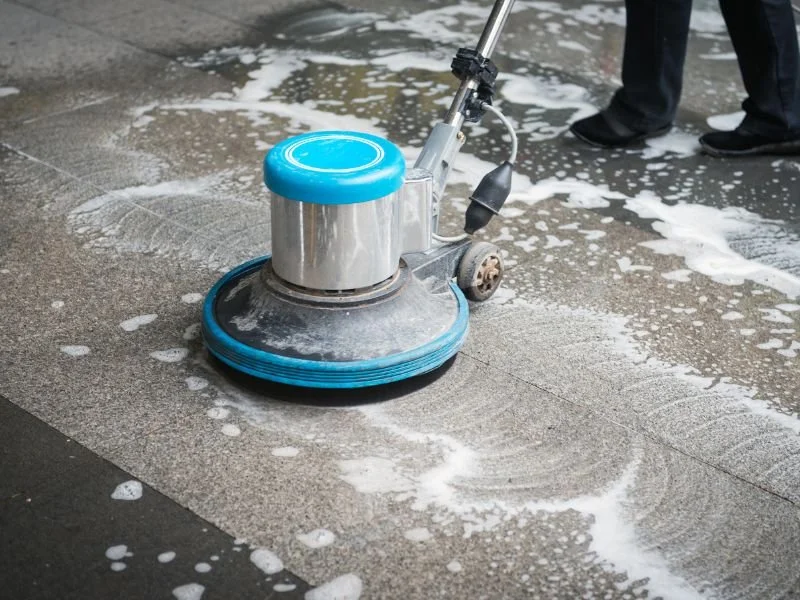 A floor cleaning machine scrubbing a wet floor with soap and bubbles.