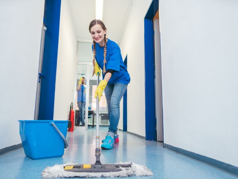 Young woman in cleaning gloves mopping a hallway in a building.