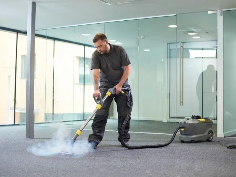 Man cleaning carpet with professional steam cleaning machine in modern office