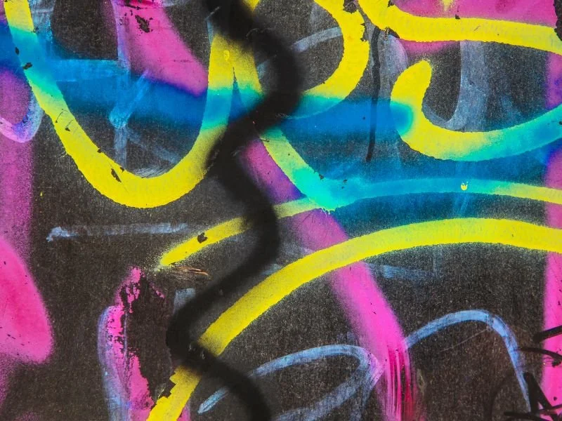 Close-up of colorful graffiti with pink, blue, yellow, and black spray paint on a wall.