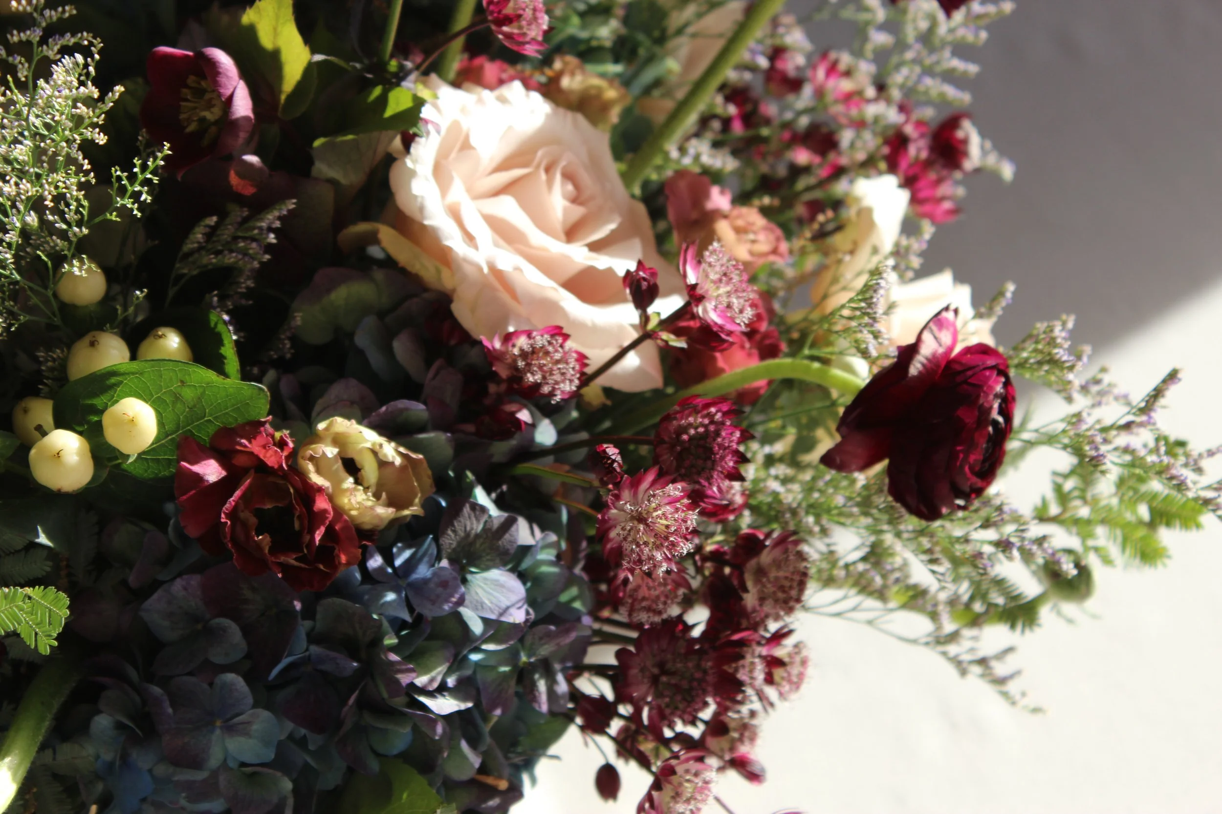 Arrangement of various flowers including a cream-colored rose, pink and red flowers, and greenery.