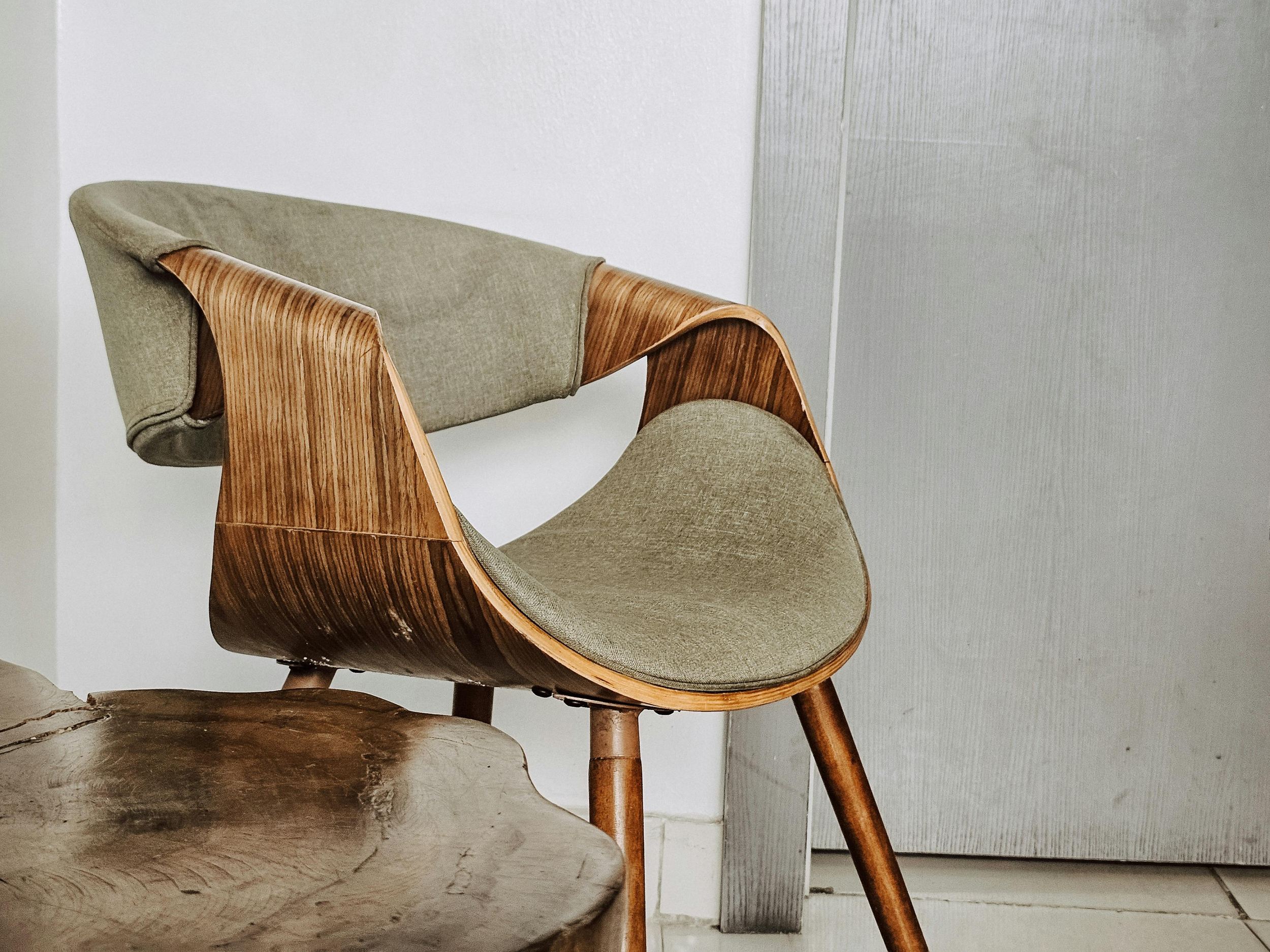 A modern wooden and fabric lounge chair with curved design, placed on tiled floor next to a small wooden table.