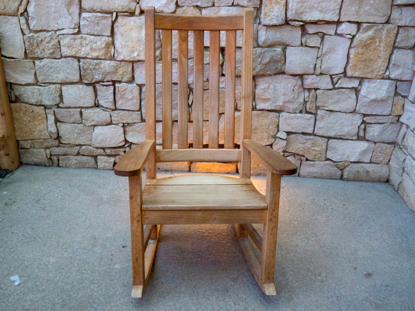 Wooden rocking chair placed on a concrete floor in front of a stone wall.