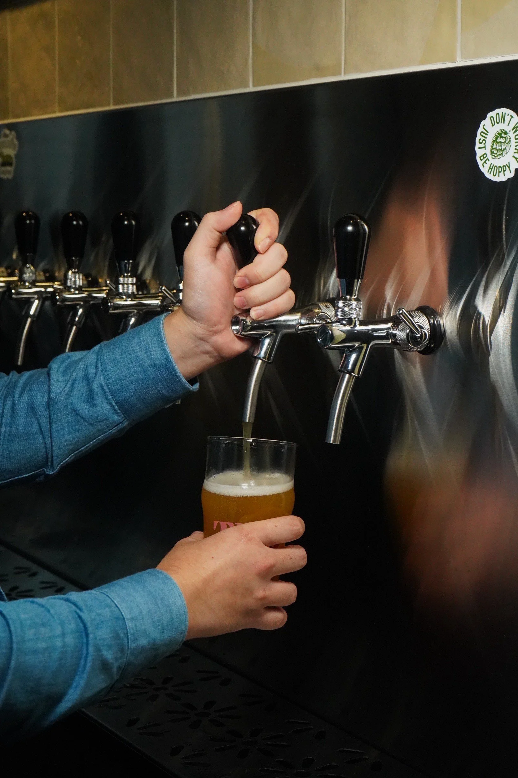 Person pouring beer from tap wall into glass at bar.