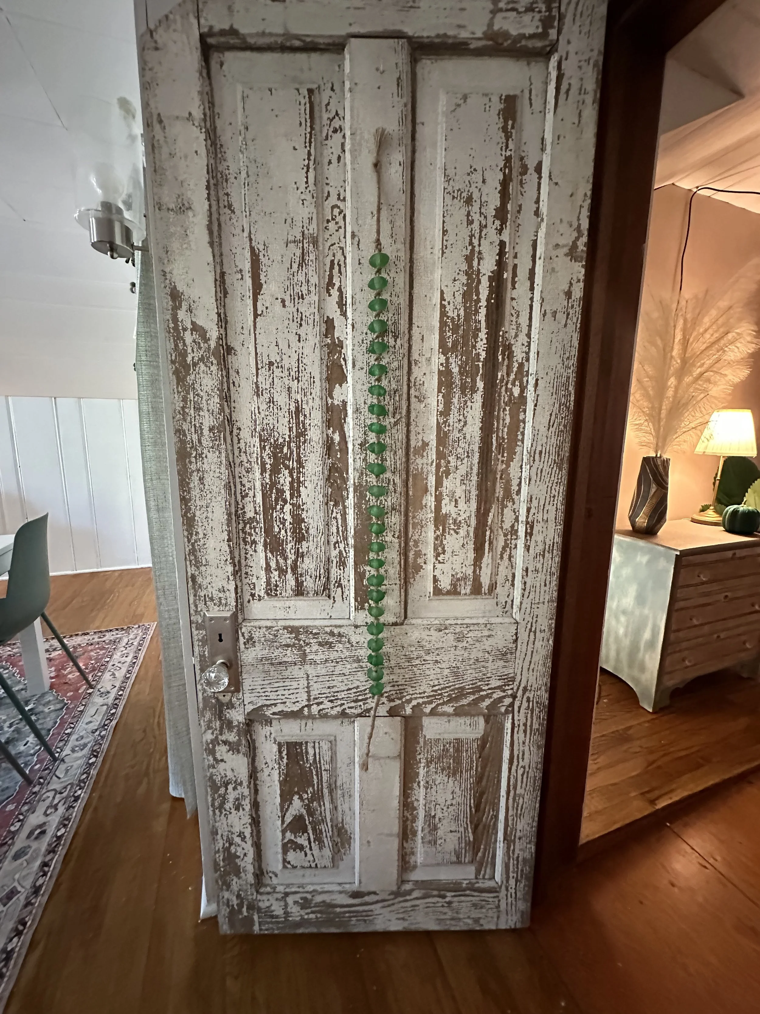 A chipped and weathered white wooden door with a green string of beads hanging from the middle.