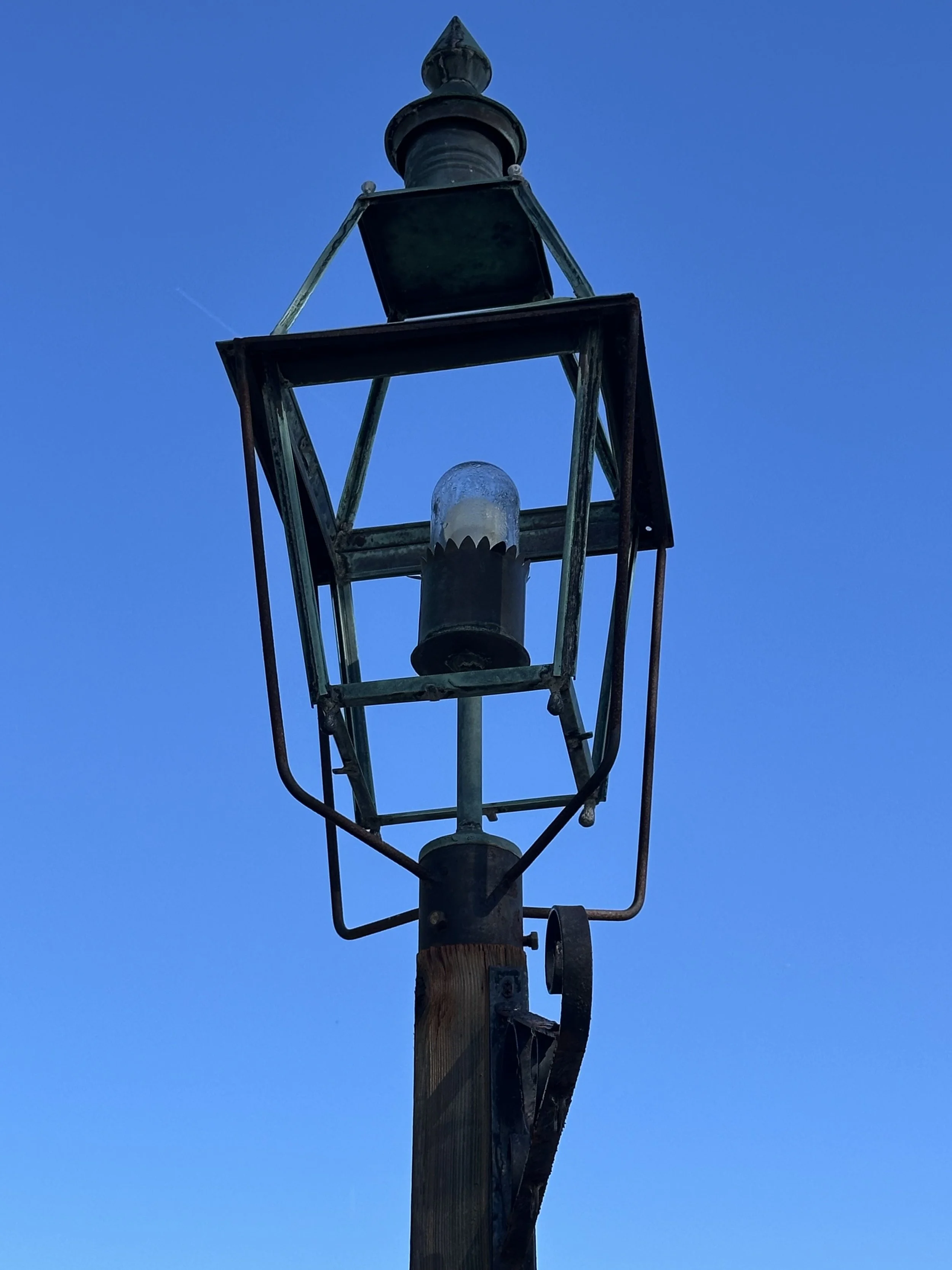 Old metal street lamp mounted on a wooden pole against a clear blue sky