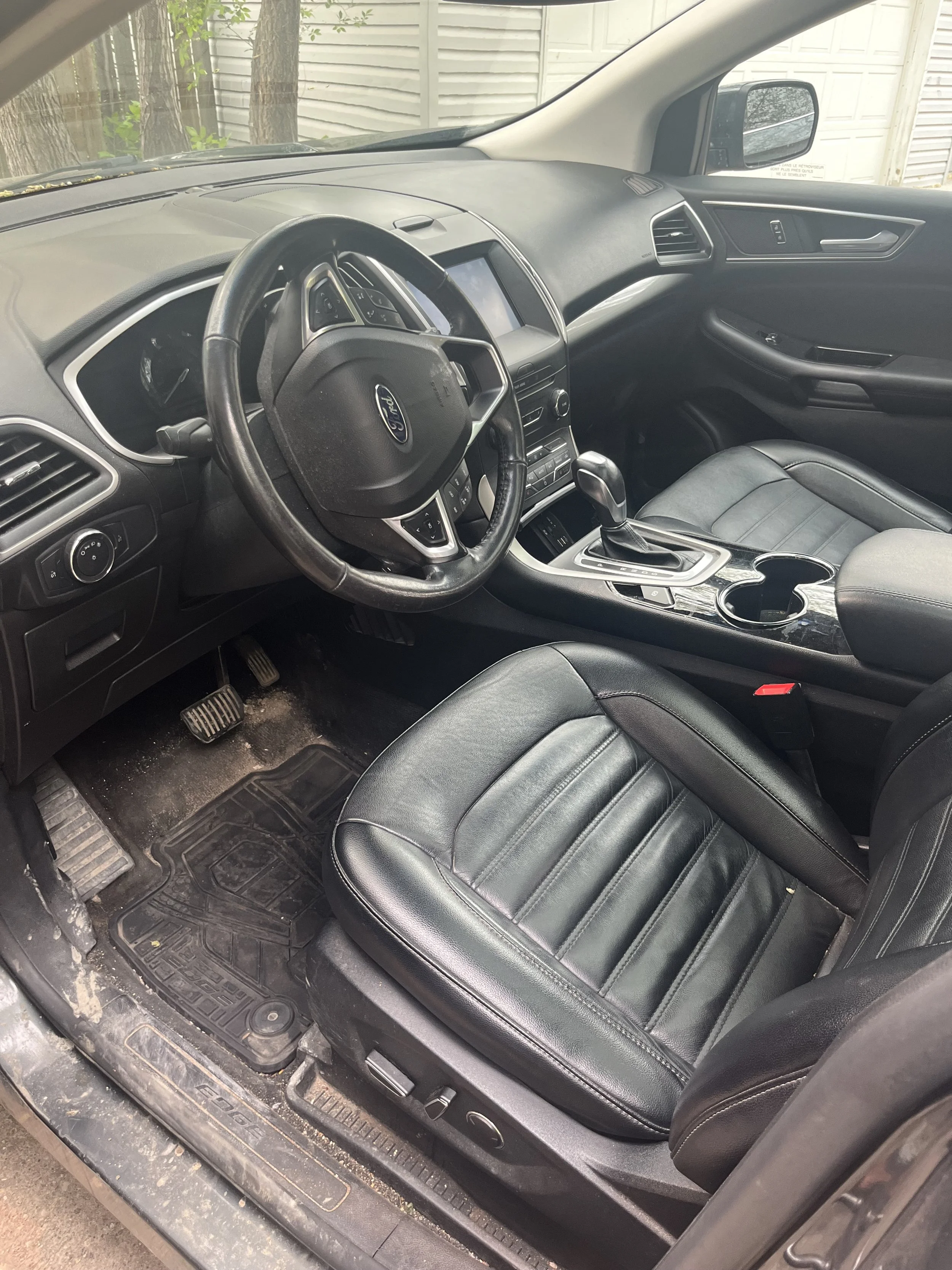 Interior of a black Ford vehicle showing the driver's seat, steering wheel, dashboard, and center console with gear shift and cup holders.