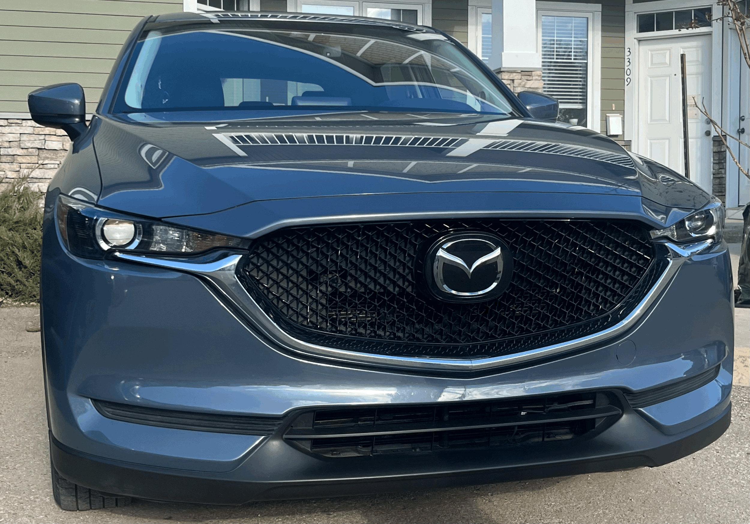 Front view of a dark blue Mazda sedan parked in front of a house.