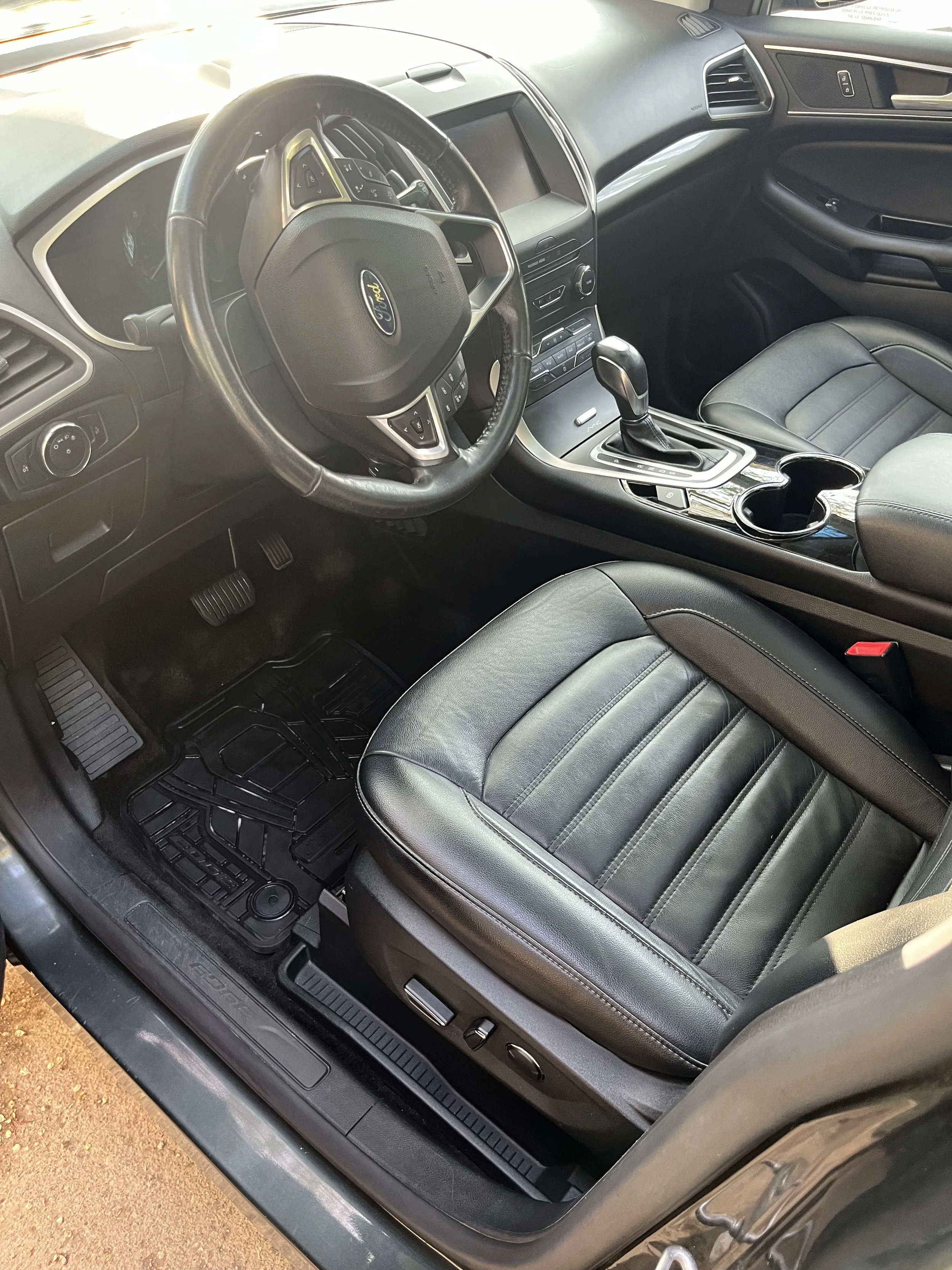 The interior of a Ford vehicle, showing the front passenger seat, the center console with cup holders, gear shift, and dashboard with controls and display screen after interior detailing process.