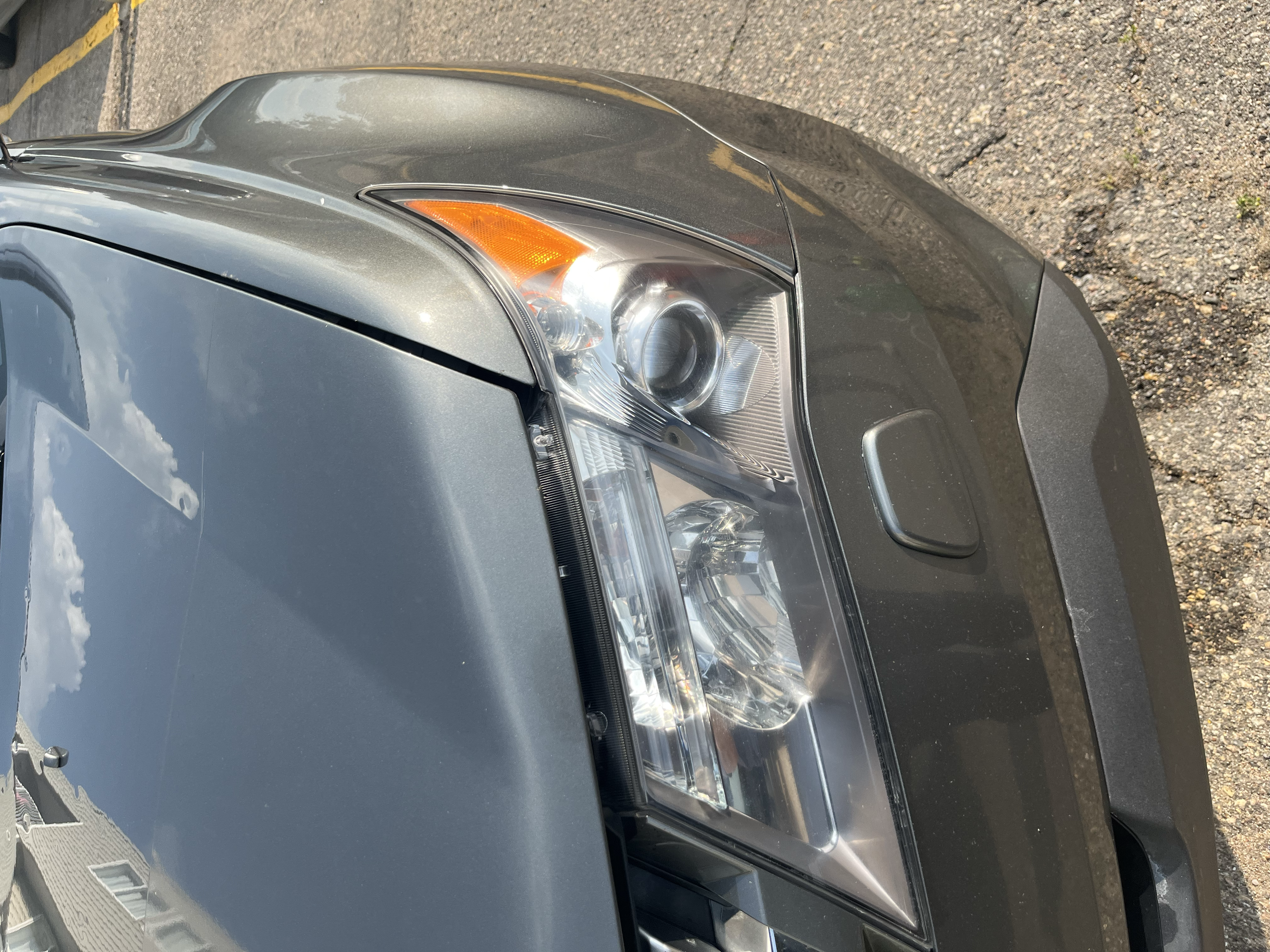 Close-up of a car's front right headlight, showing the gray body, clear lens, and a side turn signal.
