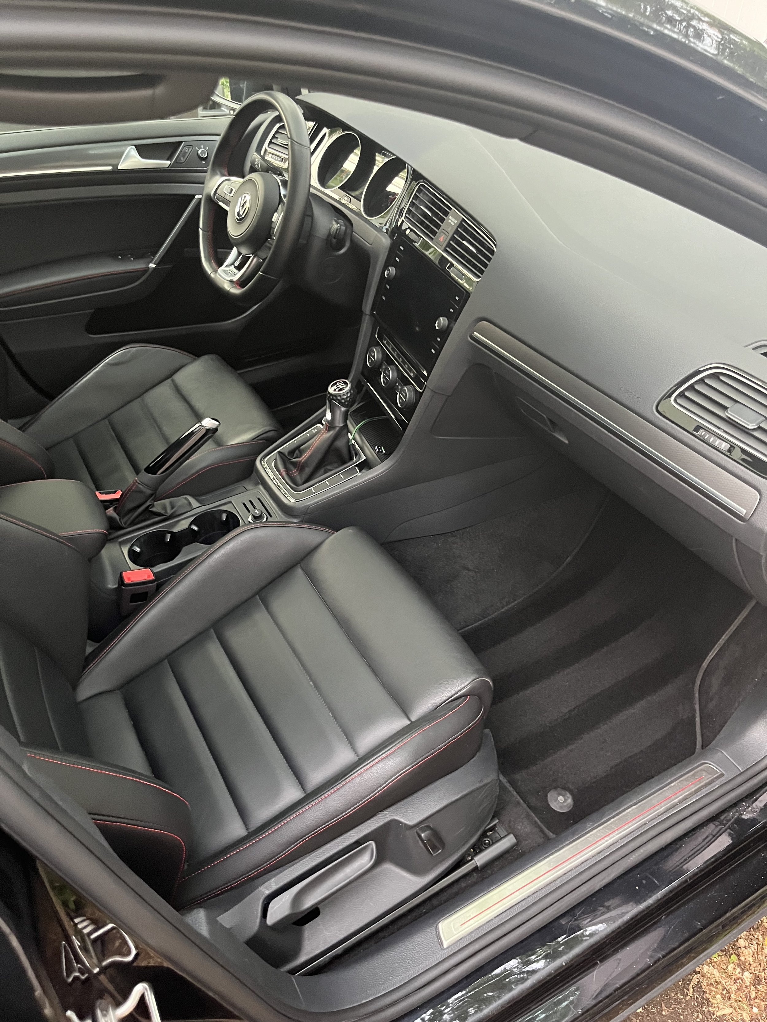 Interior view of a black Volkswagen car with manual transmission, leather seats with red stitching, and a dashboard with a touchscreen display.